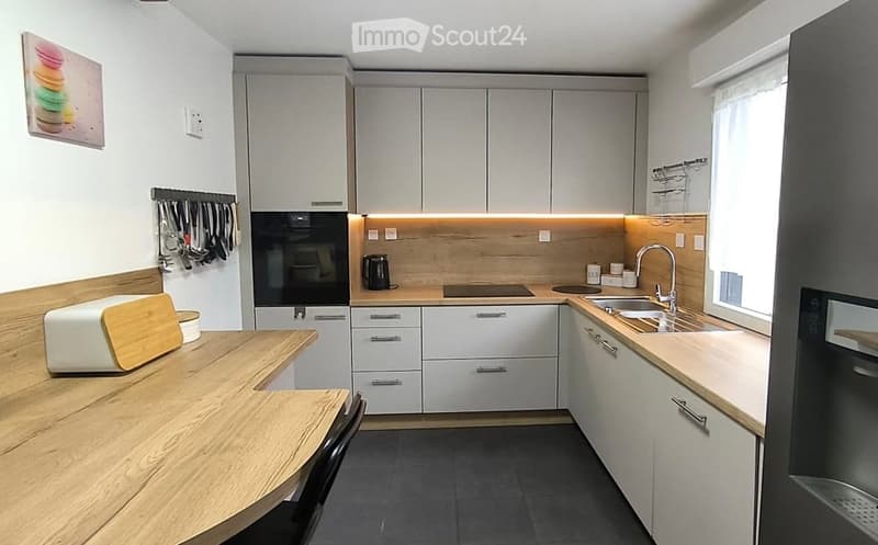 Modern kitchen with white cabinets, wooden countertops, and stainless steel appliances. Features include a built-in oven, sink with a modern faucet, and a small dining area with a wooden table and chair.
