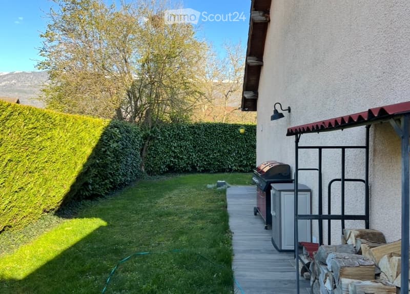 Well-maintained garden with a neatly trimmed hedge, a grassy lawn, a paved pathway, and a barbecue area with a grill and storage unit.