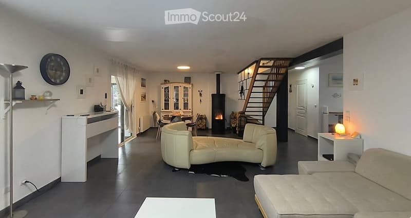 Bright living room with a fireplace, cream-colored sectional sofa, dining area with chairs and table, white cabinet, and a staircase leading to the upper level.