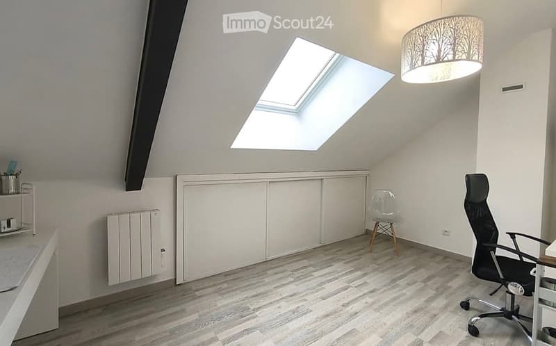 Bright attic room with wooden flooring, white walls, built-in cabinetry, a large skylight, a modern hanging lamp, and a black office chair.
