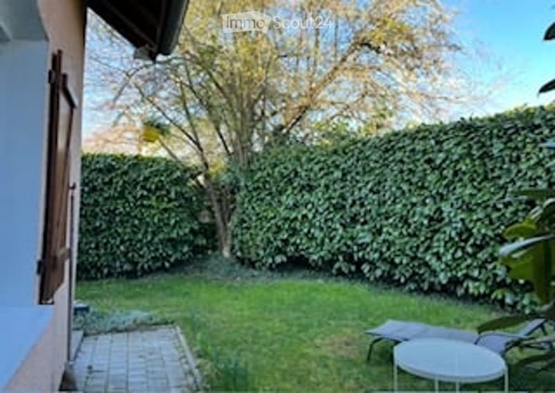 Private garden with neatly trimmed hedge, small patio area, lounge chairs, and a small table.