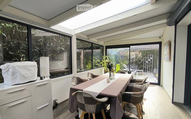 Bright, airy dining area with large windows and sliding glass doors leading to a terrace. Features a dining table with chairs, a cabinet, and a lamp.