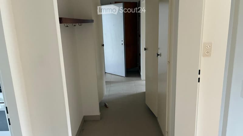 Empty hallway with tiled floor, white walls, and a closed door leading to another room.