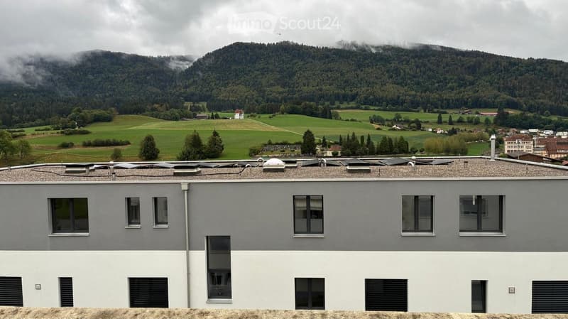 Modern two-story building with grey and white facade, multiple windows, and a flat roof with solar panels.