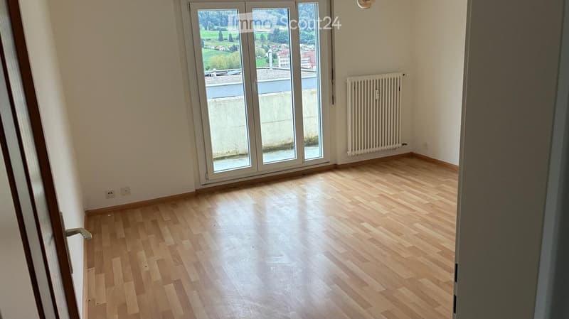 Empty room with wooden flooring, large sliding glass doors, and a radiator on the wall.