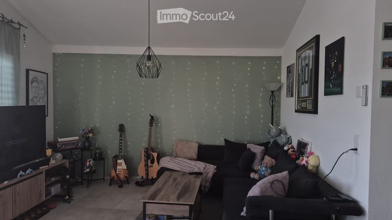 Living room with a dark grey sofa, wooden coffee table, two guitars, a small table with a lamp, and several picture frames on the walls.