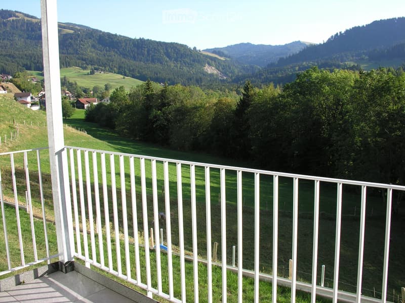 Balcony with white metal railing overlooking a green valley with scattered houses and forested hills.