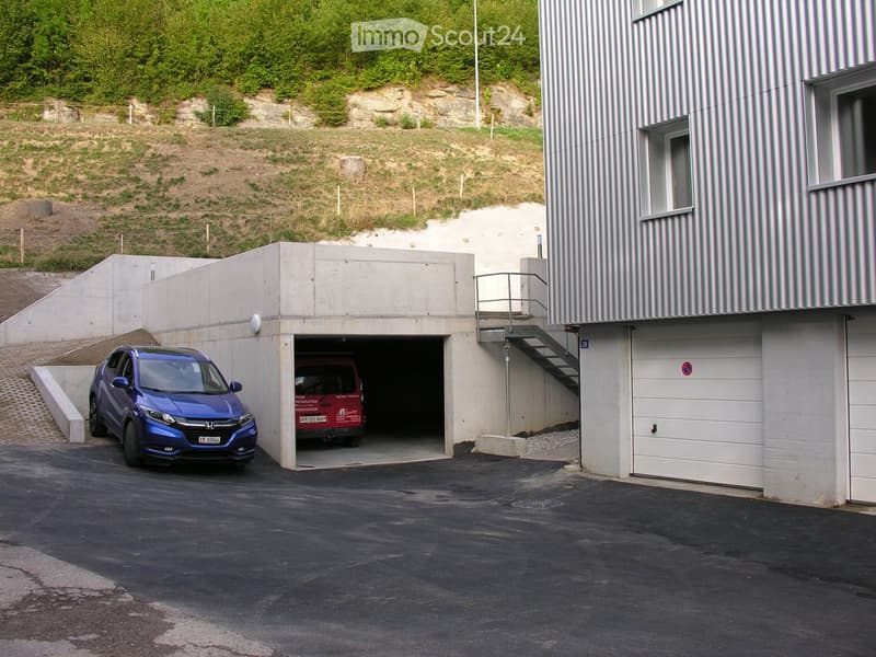 Modern building with a covered garage area, two parked cars, and a staircase leading to an upper level.