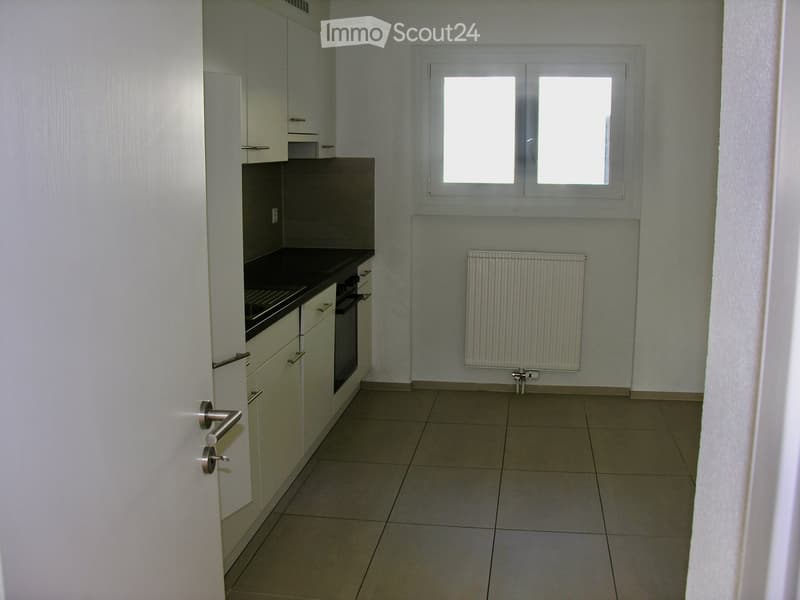 Empty kitchen with white cabinets, black countertop, tiled floor, and a window with two panes.