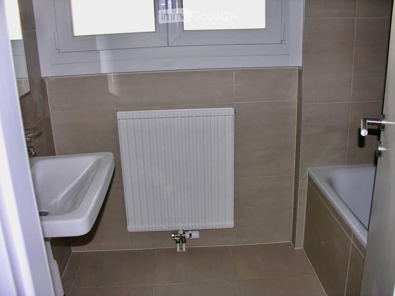 Bathroom with beige tiled walls and floor, a white sink, a bathtub, and a radiator.