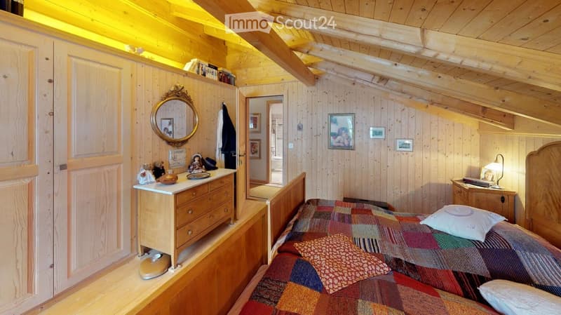 Cozy wooden bedroom with slanted ceilings, a single bed with a colorful quilt, a nightstand with a lamp, a dresser with a mirror, and decorative items on the walls.