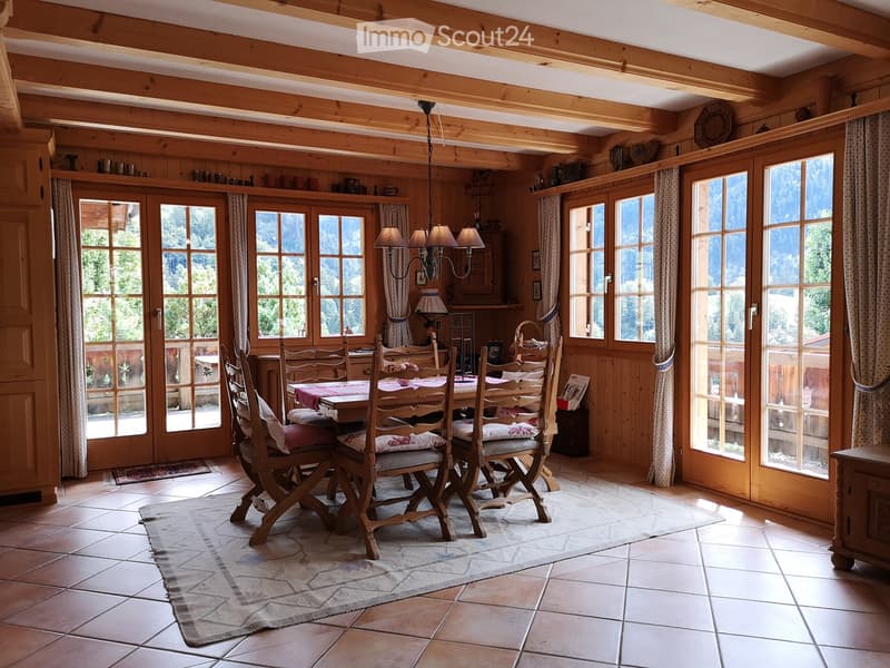 Cozy dining room with wooden beams, large windows, and a dining set with six chairs around a table.