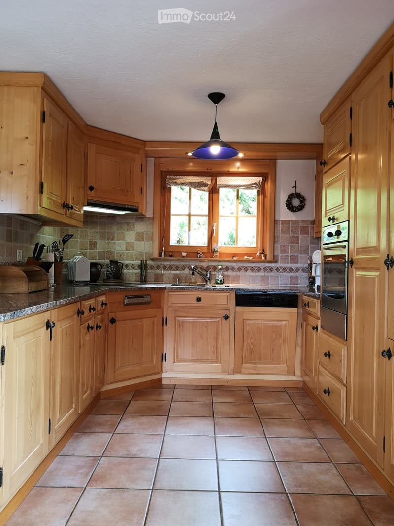 Bright, airy kitchen with light wooden cabinets, granite countertops, and tiled flooring. Features an oven, dishwasher, and a pendant light fixture.