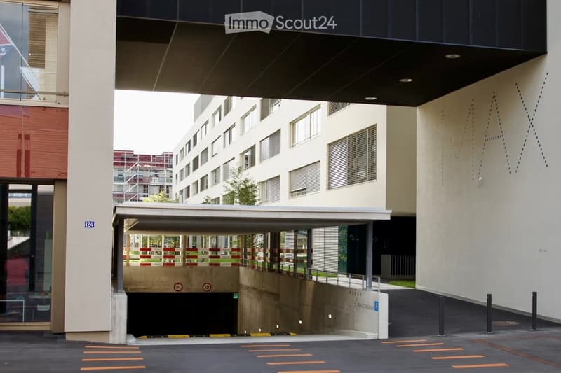 Modern multi-story building with a covered entrance and parking area. Features include a raised ground floor, glass windows, and a clean, contemporary design.