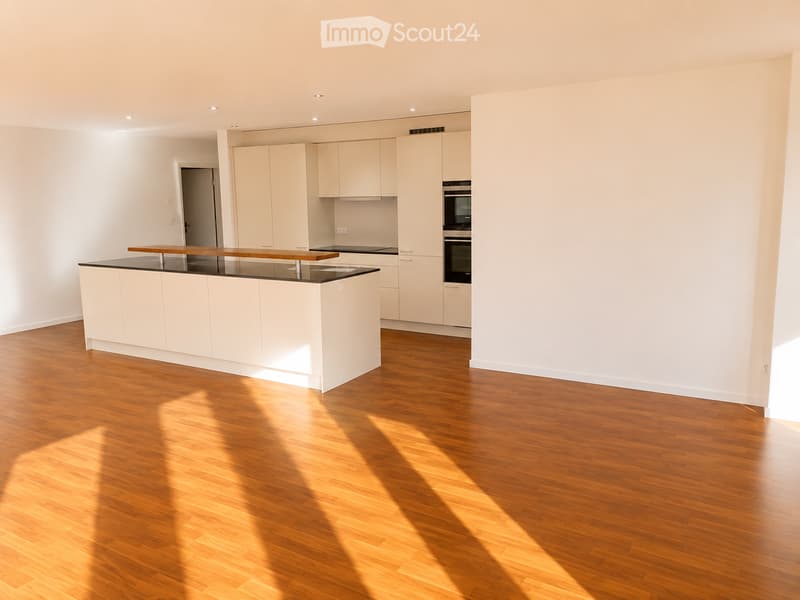 Modern kitchen with white cabinets, a central island with a wooden countertop, and a built-in oven. The floor is made of polished wood, and the walls are painted white.