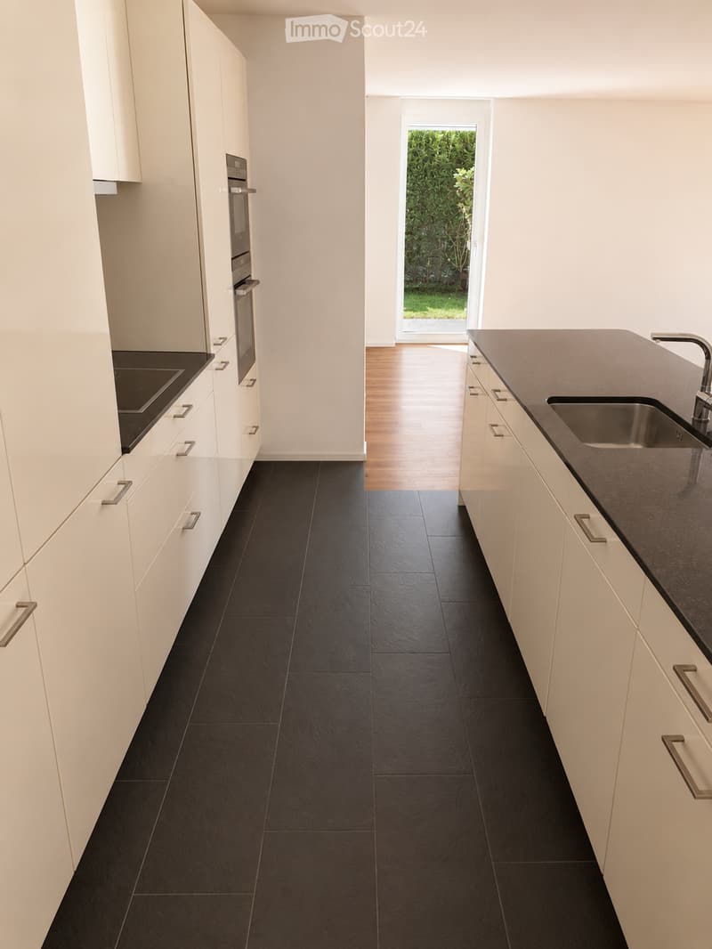 Modern kitchen with white cabinets, black countertops, and black tiled flooring. Features a stainless steel sink and oven.