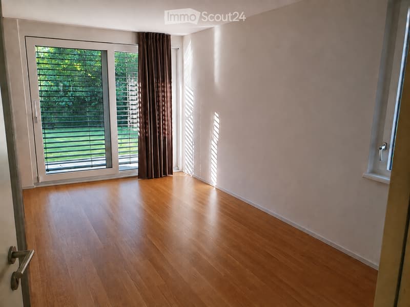 Empty room with wooden flooring, large windows, and sliding glass doors leading to a balcony.