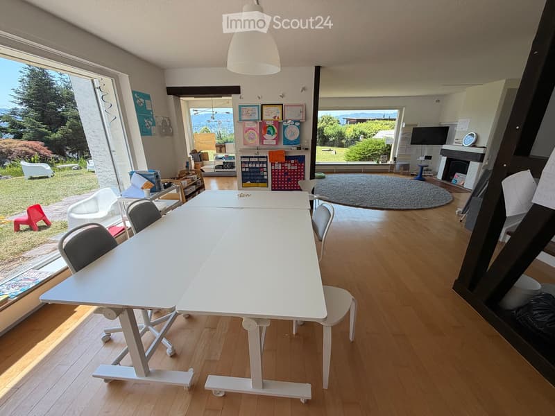Bright room with wooden flooring, large windows, a white table with chairs, a fireplace, and a round rug.