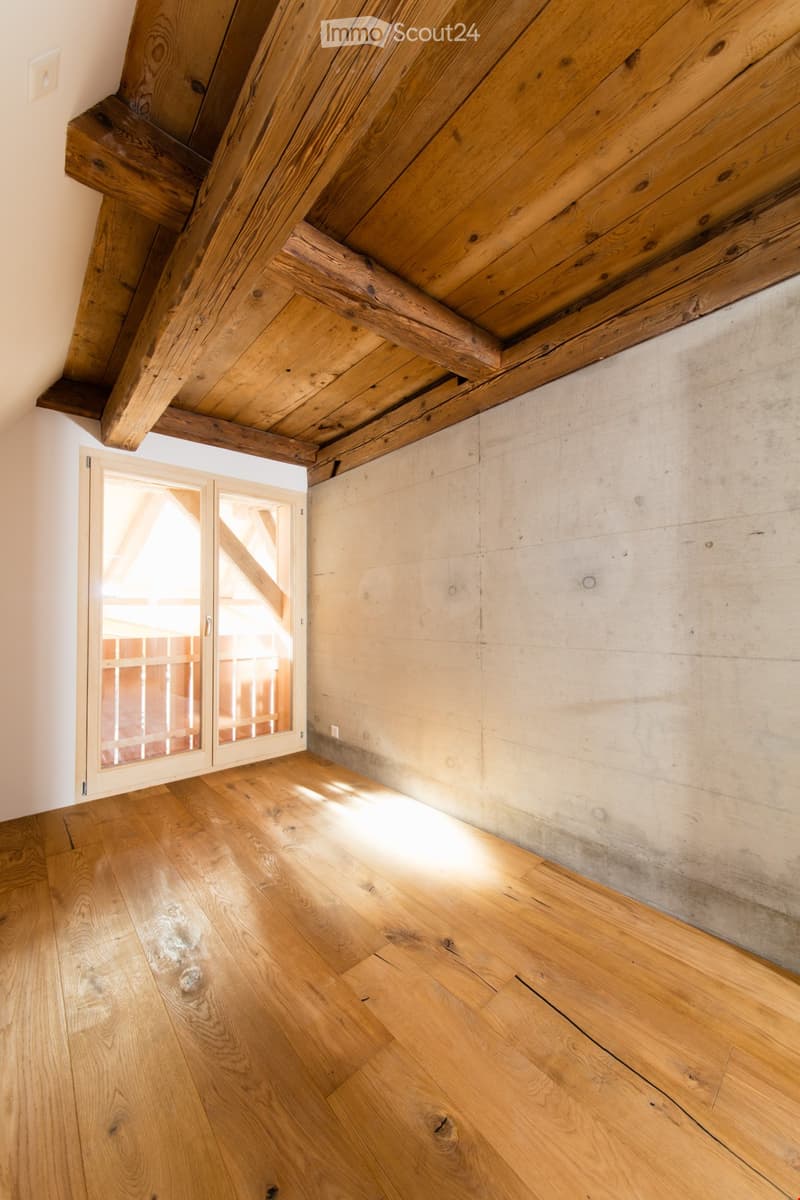 Empty room with wooden floor, exposed wooden beams on the ceiling, and a glass door leading outside.