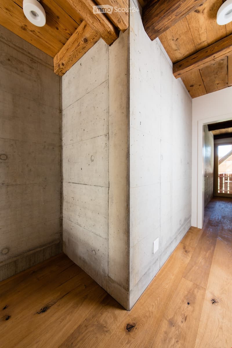 Modern hallway with exposed wooden beams on the ceiling, polished wooden flooring, and textured concrete walls.