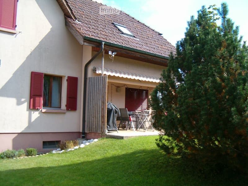 Two-story house with beige walls, red shutters, and a covered patio area with outdoor furniture.