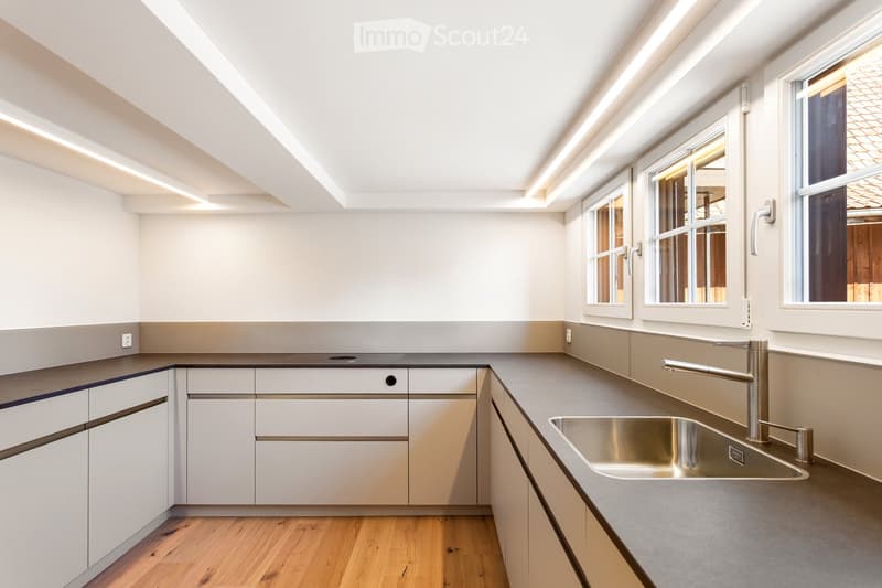 Modern kitchen with white cabinets, stainless steel sink, and sleek faucet. Natural light from large windows illuminates the space.