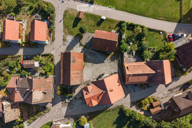Aerial view of a residential neighborhood with multiple houses featuring red-tiled roofs, surrounded by greenery and roads.