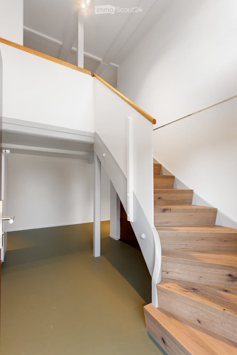 Modern hallway with a wooden staircase, white walls, and a glass door leading to another room. The floor is painted in a muted green color, and the staircase features a wooden handrail and steps.