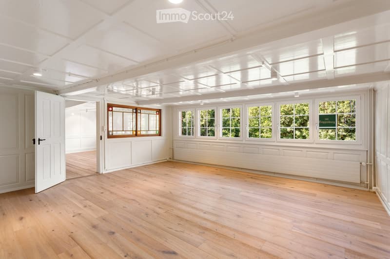 Empty room with wooden flooring, white walls, large windows, and a radiator. No furniture or equipment present.