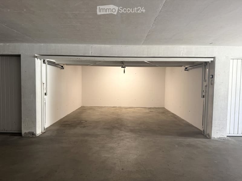 Empty underground parking space with concrete floor and walls, two open garage doors, and minimal lighting.