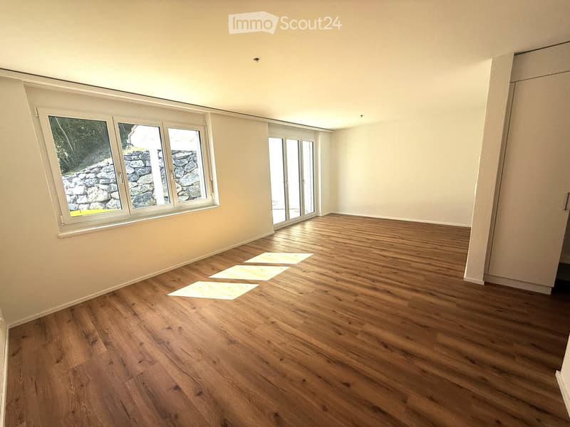 Empty room with wooden flooring, large windows, and sliding glass doors leading outside.