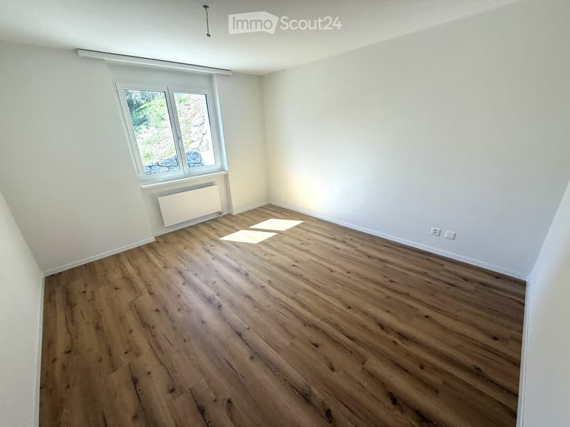 Empty room with wooden flooring, white walls, and a window with a view of greenery. No furniture or equipment is present.