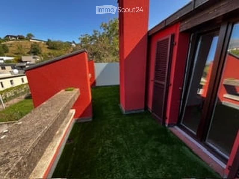 Balcony with artificial grass, red walls, large windows, and scenic hillside view.