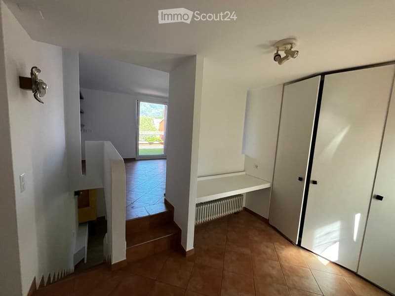 Empty hallway with tiled floor, white walls, built-in storage, and a staircase leading to another room.