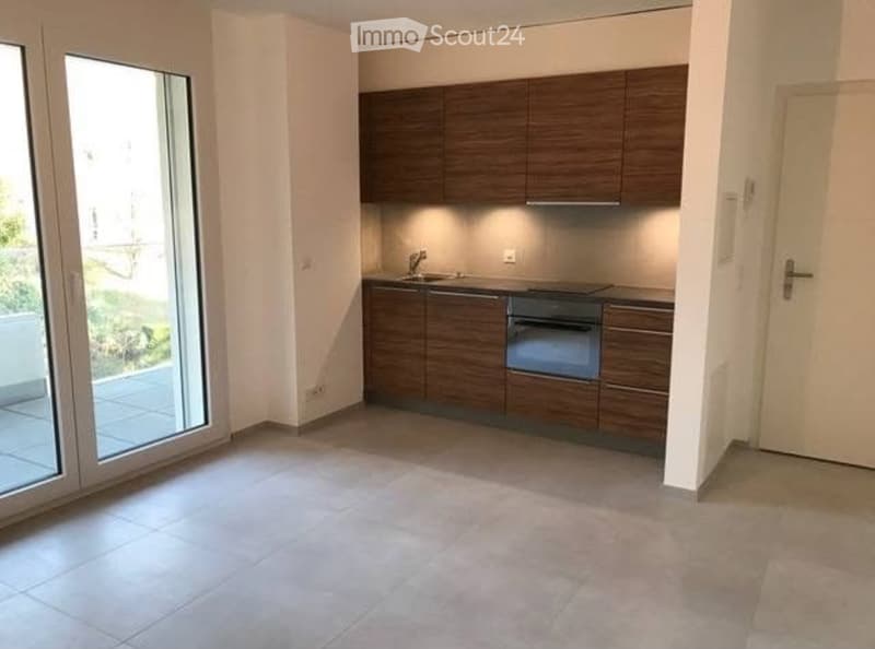 Modern kitchen with dark wooden cabinets, a sink, and an oven. The space is open and bright, with large windows and a tiled floor.