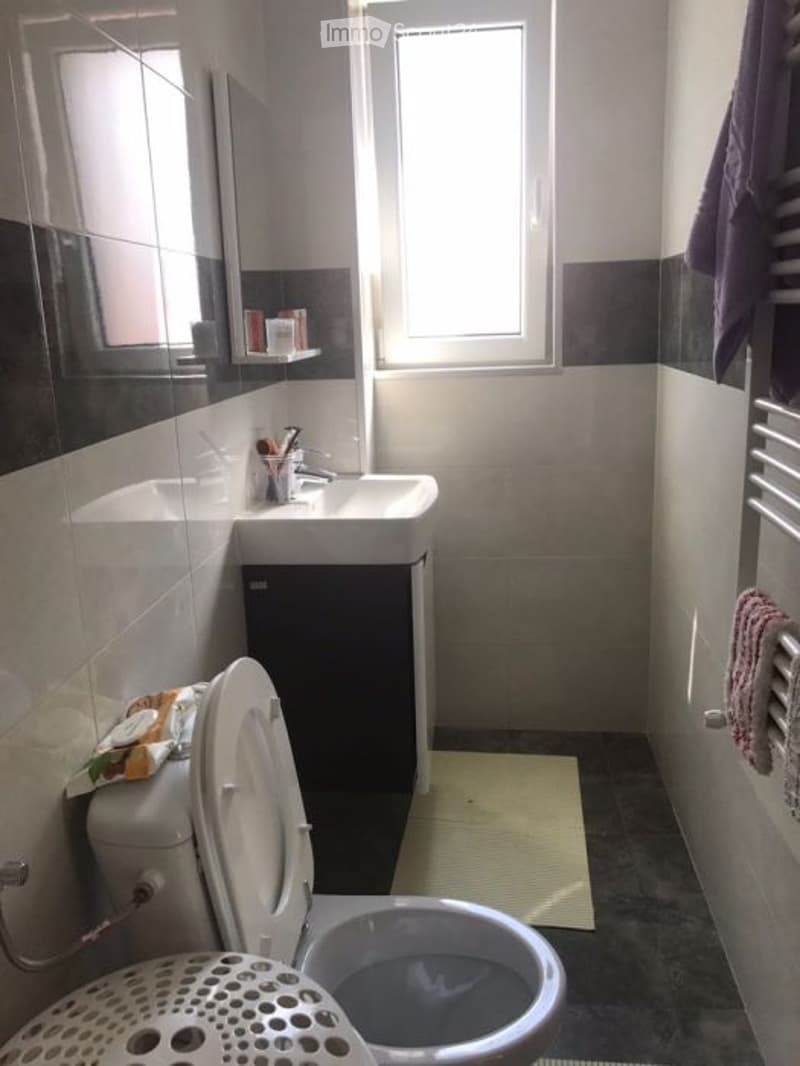 Modern bathroom with a sink, mirror, toilet, and shower. The walls are tiled in a combination of dark and light colors, and there is a towel hanging on the side.
