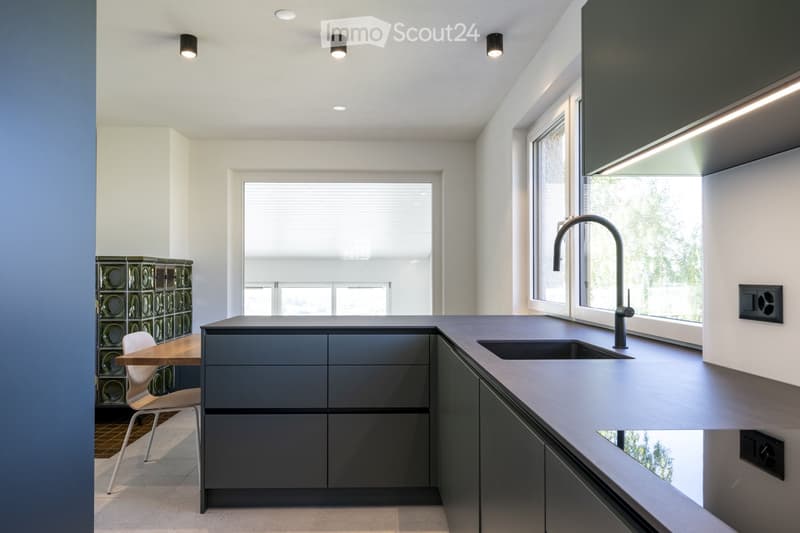 Modern kitchen with grey cabinets, a central island, a sink with a modern faucet, a small table with a chair, and a decorative glass block wall.