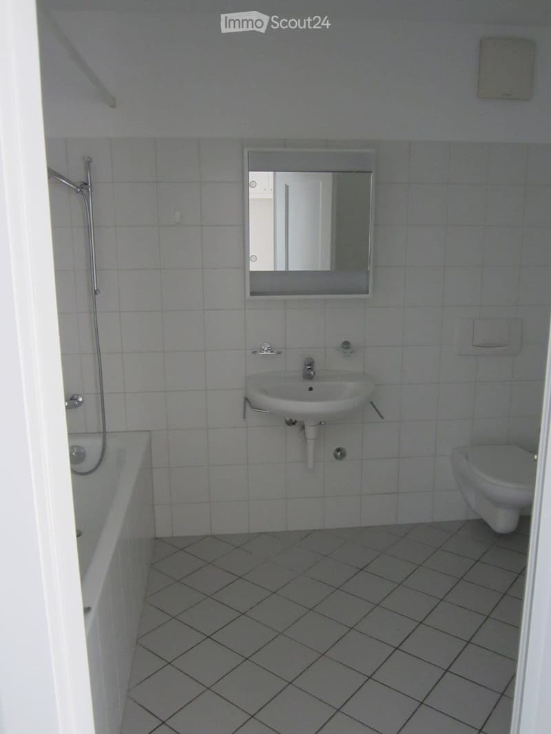 Clean, modern bathroom with white tiles, a sink, toilet, bathtub, and a mirror above the sink.