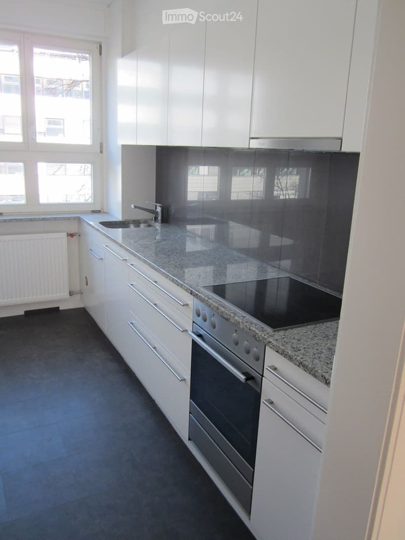 Modern kitchen with white cabinets, granite countertop, built-in oven, sink, and faucet. Large windows provide natural light.