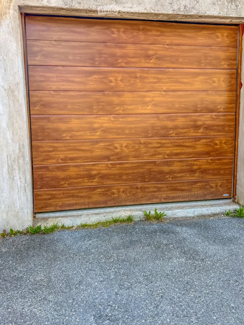 Wooden garage door with horizontal slats, mounted on a concrete wall, with small patches of grass growing near the base.