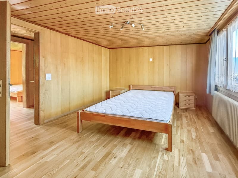 Cozy bedroom with wooden walls and floor, featuring a single bed, nightstands, and a radiator.