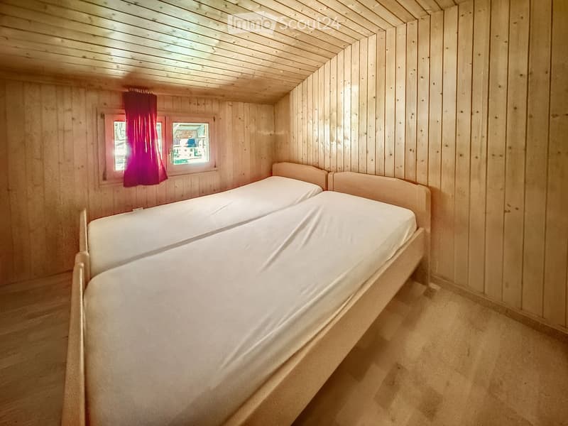 Cozy wooden bedroom with a single bed, red curtain, and small window.
