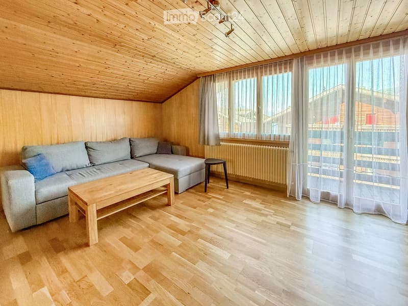 Living room with wooden walls and ceiling, large windows, grey sofa, wooden coffee table, and a small black stool.