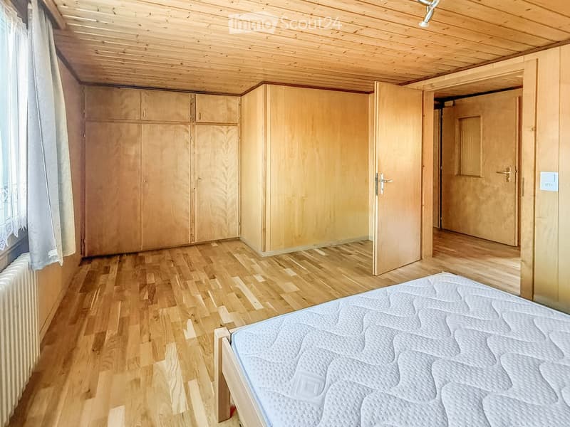 Bright bedroom with wooden flooring, a large bed, and built-in wooden wardrobes.