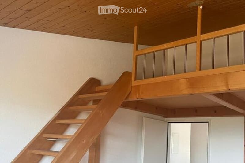 An unfurnished room with a wooden staircase leading to an upper level, featuring a wooden railing and a simple white door at the top.