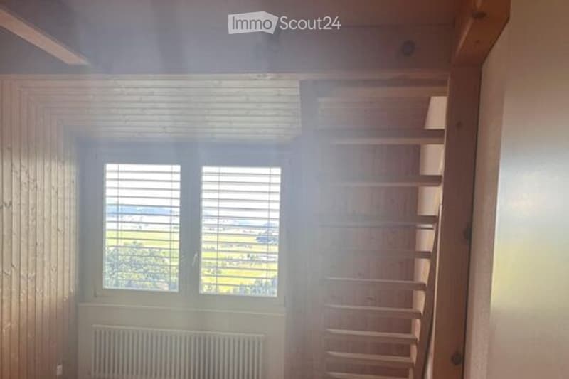 Empty room with wooden walls, large window with blinds, radiator, and built-in wooden shelving unit.