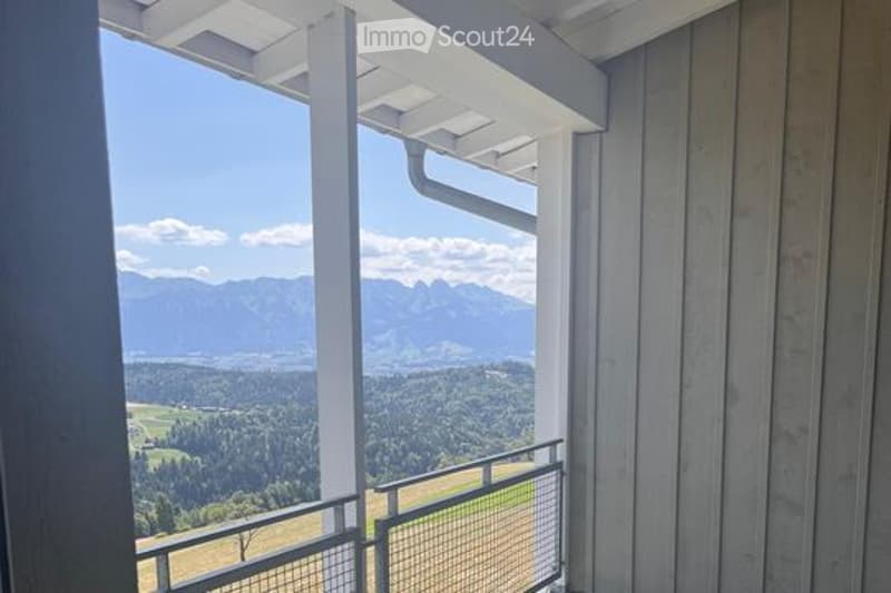 Balcony with a scenic mountain and valley view, white railings, and wooden decking.
