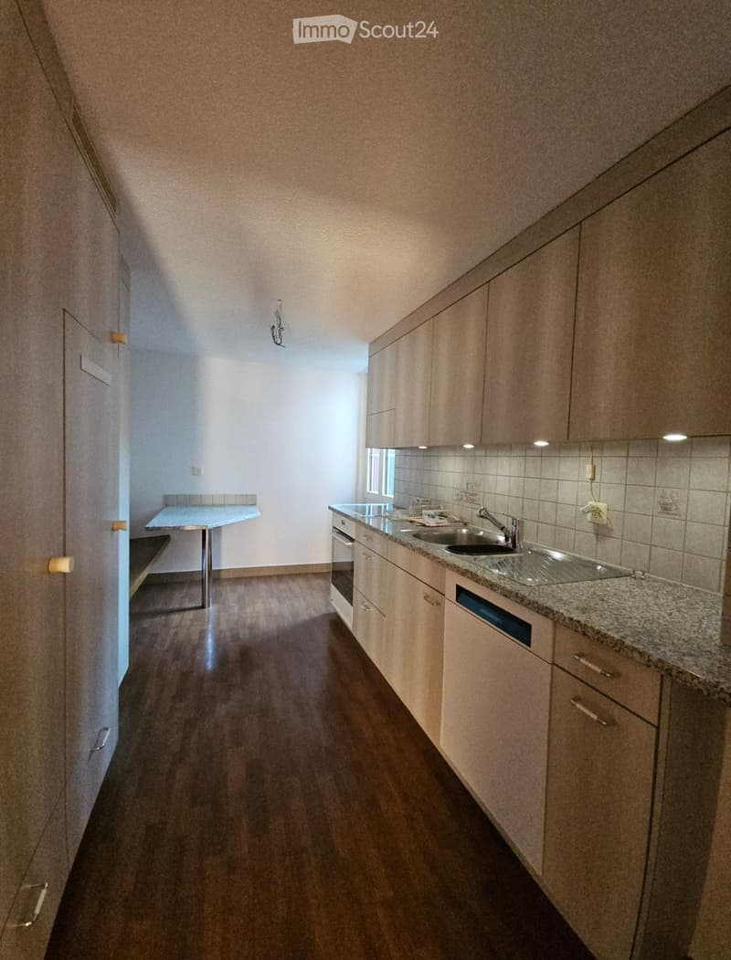 Modern kitchen with light wooden cabinets, granite countertop, sink, and a small table in the adjacent area.