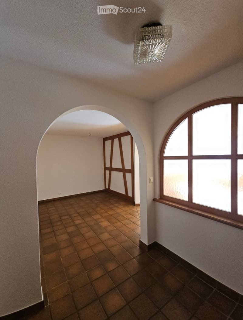 Empty hallway with arched doorways, tiled floor, and large windows on one side.