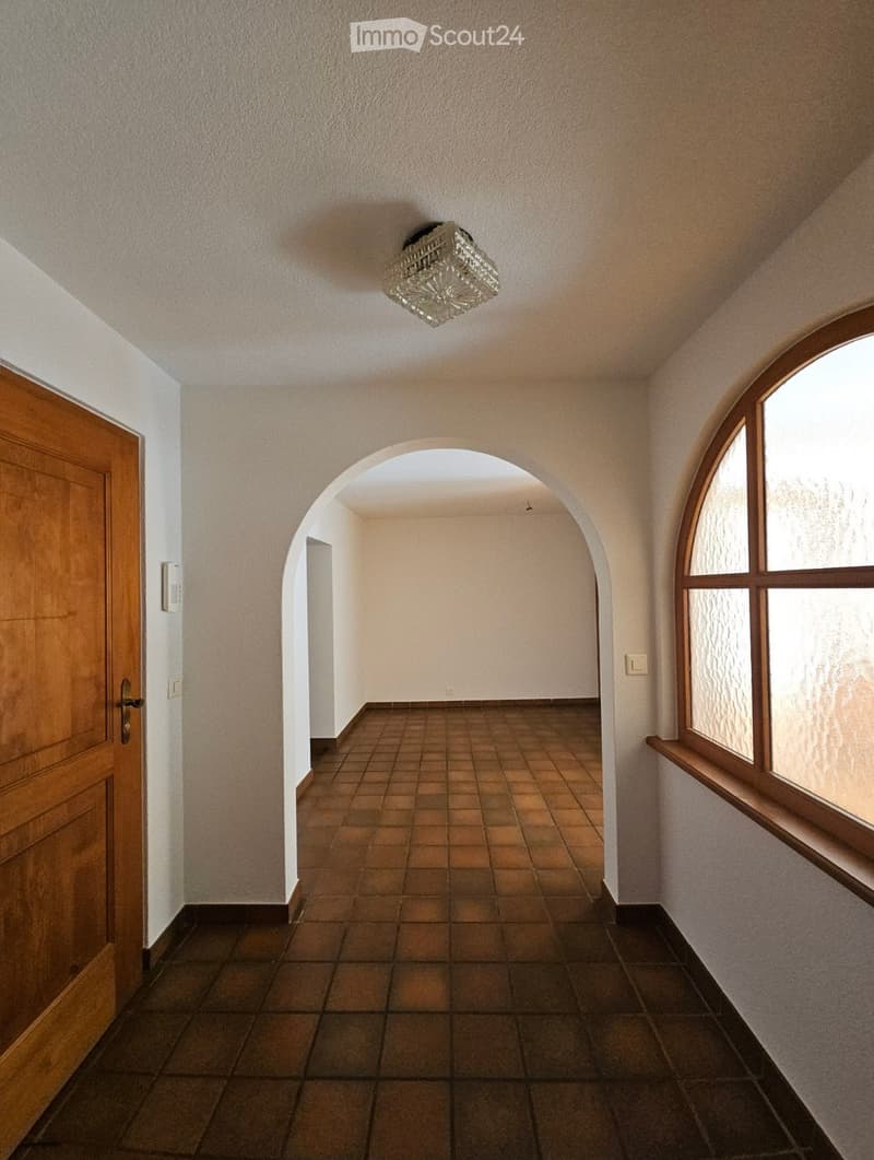 Empty hallway with tiled floor, arched passageway, wooden door, and large window with frosted glass panels.